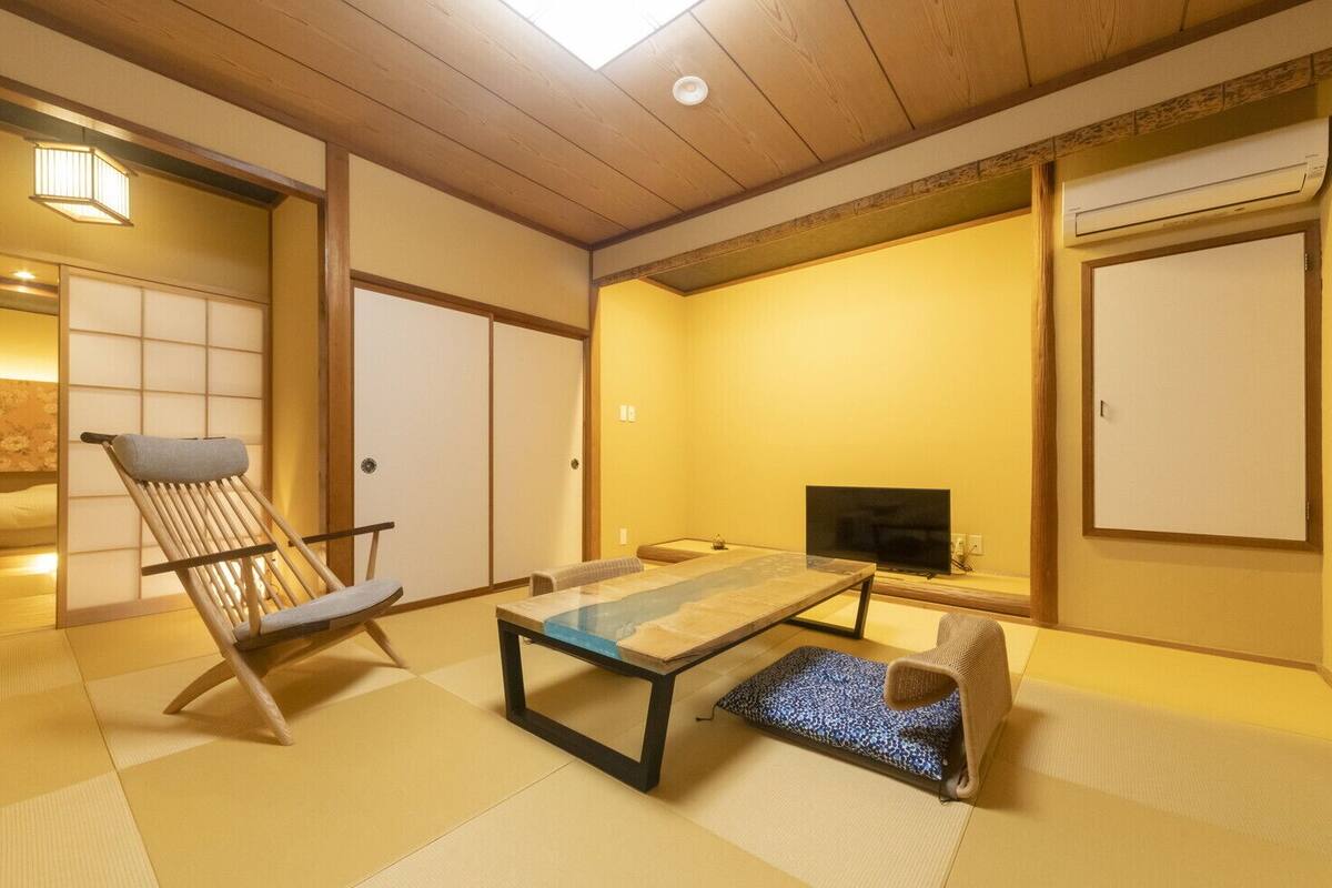 A traditional Japanese room with tatami flooring, a low table, a television, and sliding doors.