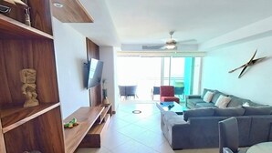 Een moderne woonkamer met een houten boekenkast, een grijze bank en een aan de muur bevestigde televisie.