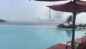 Een zwembadterras met ligbedden en parasols, met uitzicht op een helderblauw zwembad en de oceaan.
