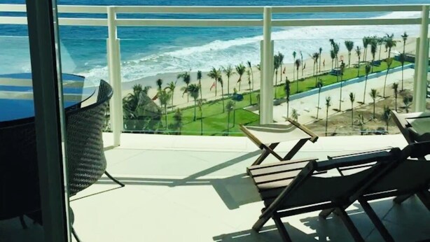 Een balkon met uitzicht op de oceaan, het strand en palmbomen.