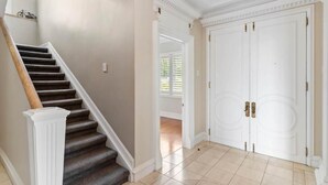 Una escalera con barandilla de madera y base blanca, que conduce a una habitación con puerta blanca y una ventana con persianas.