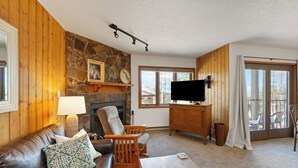 Ein gemütliches Wohnzimmer mit Kamin aus Stein, Holzwänden, einer Ledersofa und einem Flachbildfernseher.