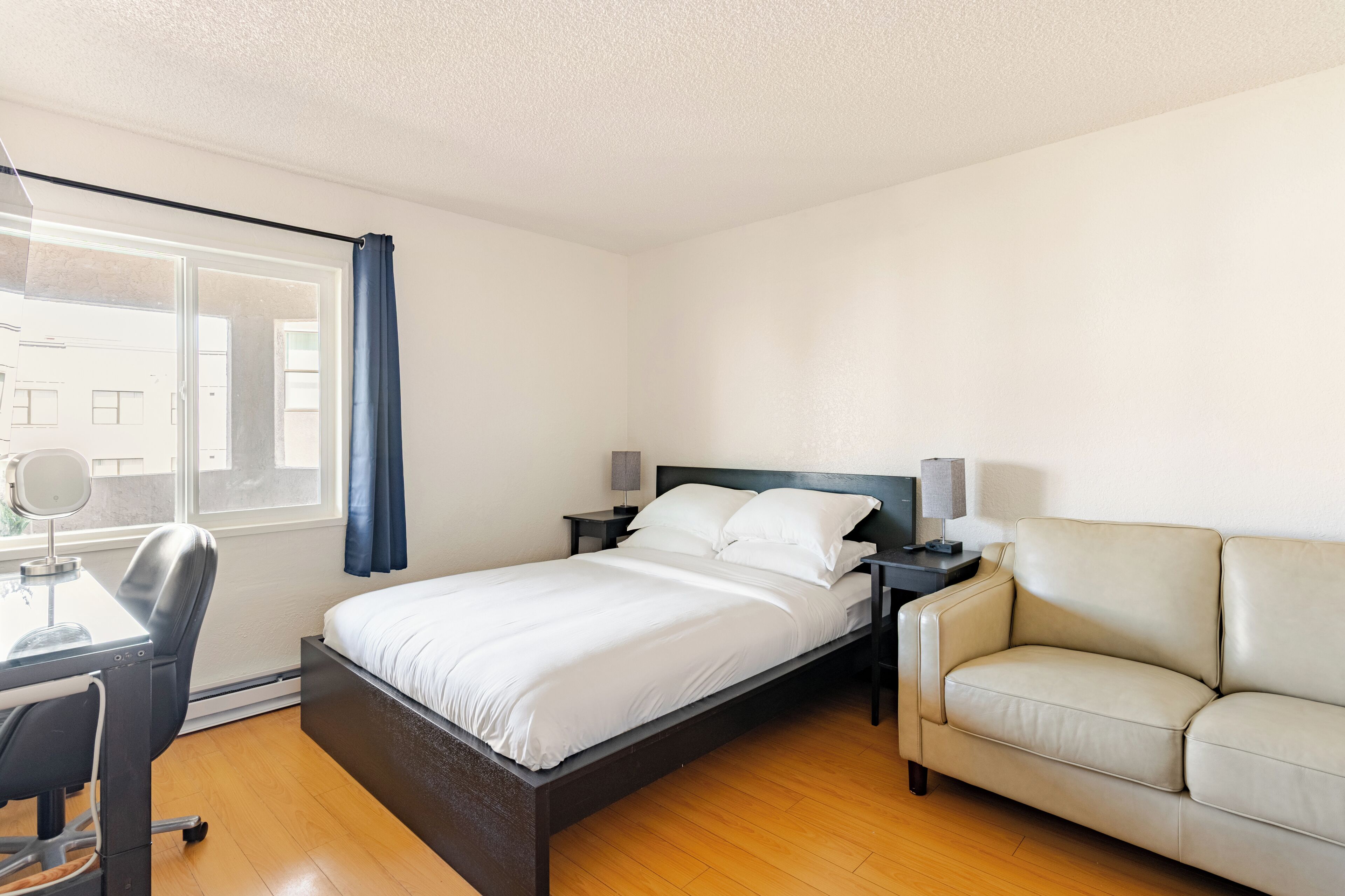 A bedroom with a bed, a desk, a chair, a nightstand, and a sofa.
