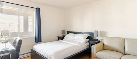 A bedroom with a bed, a desk, a chair, a nightstand, and a sofa.