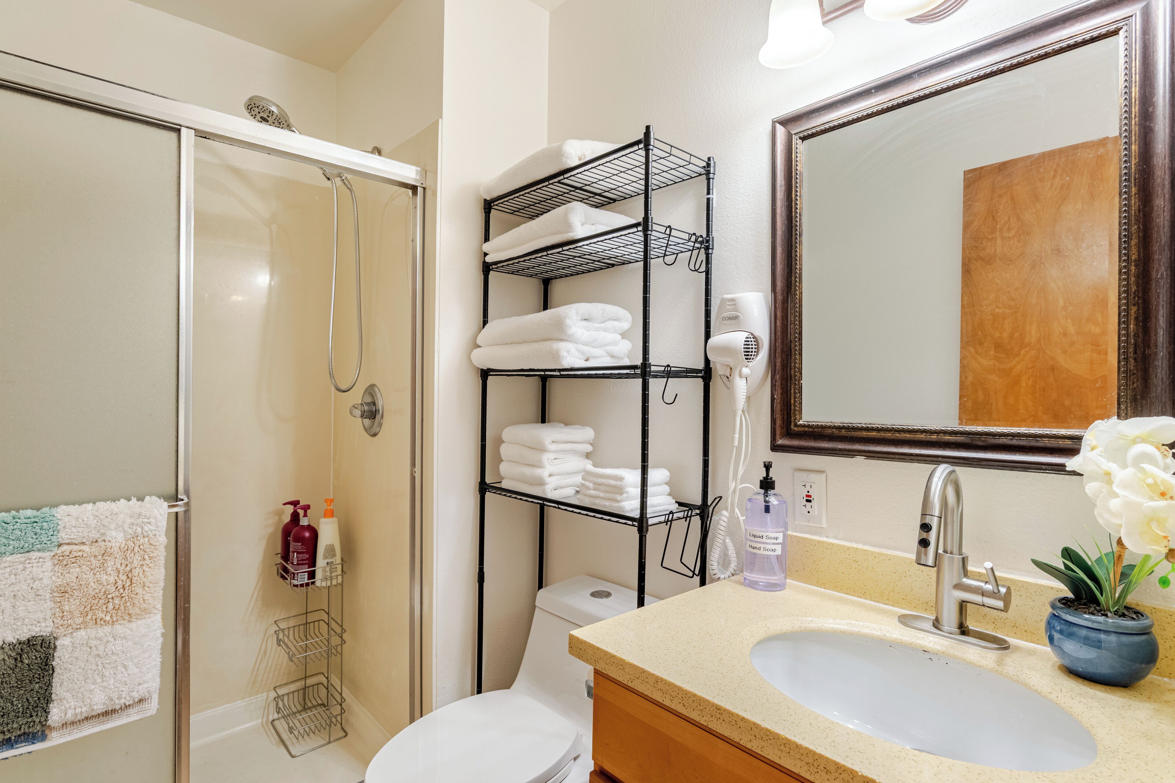 A bathroom with a shower, toilet, sink, and a towel rack with folded towels.