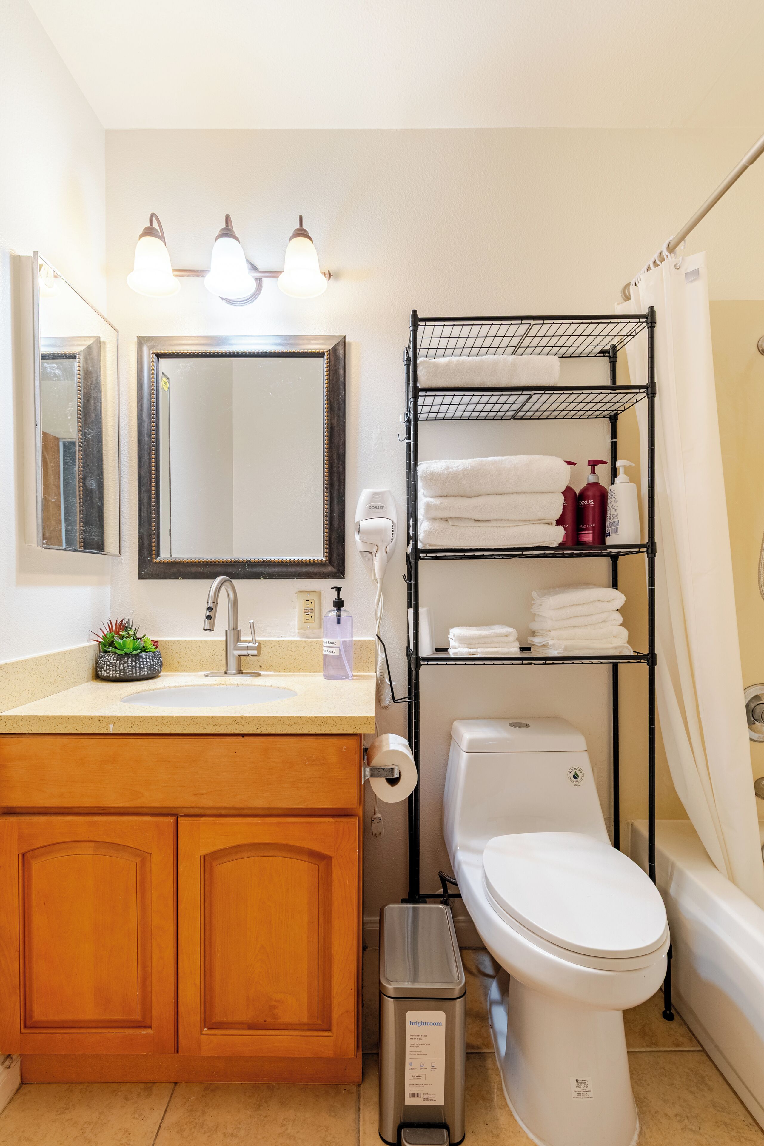 A bathroom with a wooden vanity, a sink, a mirror, a toilet, a shelf with towels, and a shower curtain.