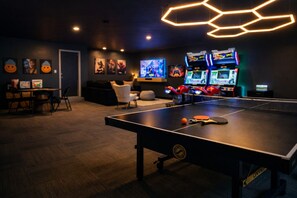 Una stanza con tavolo da ping pong, console per videogiochi e un divano.