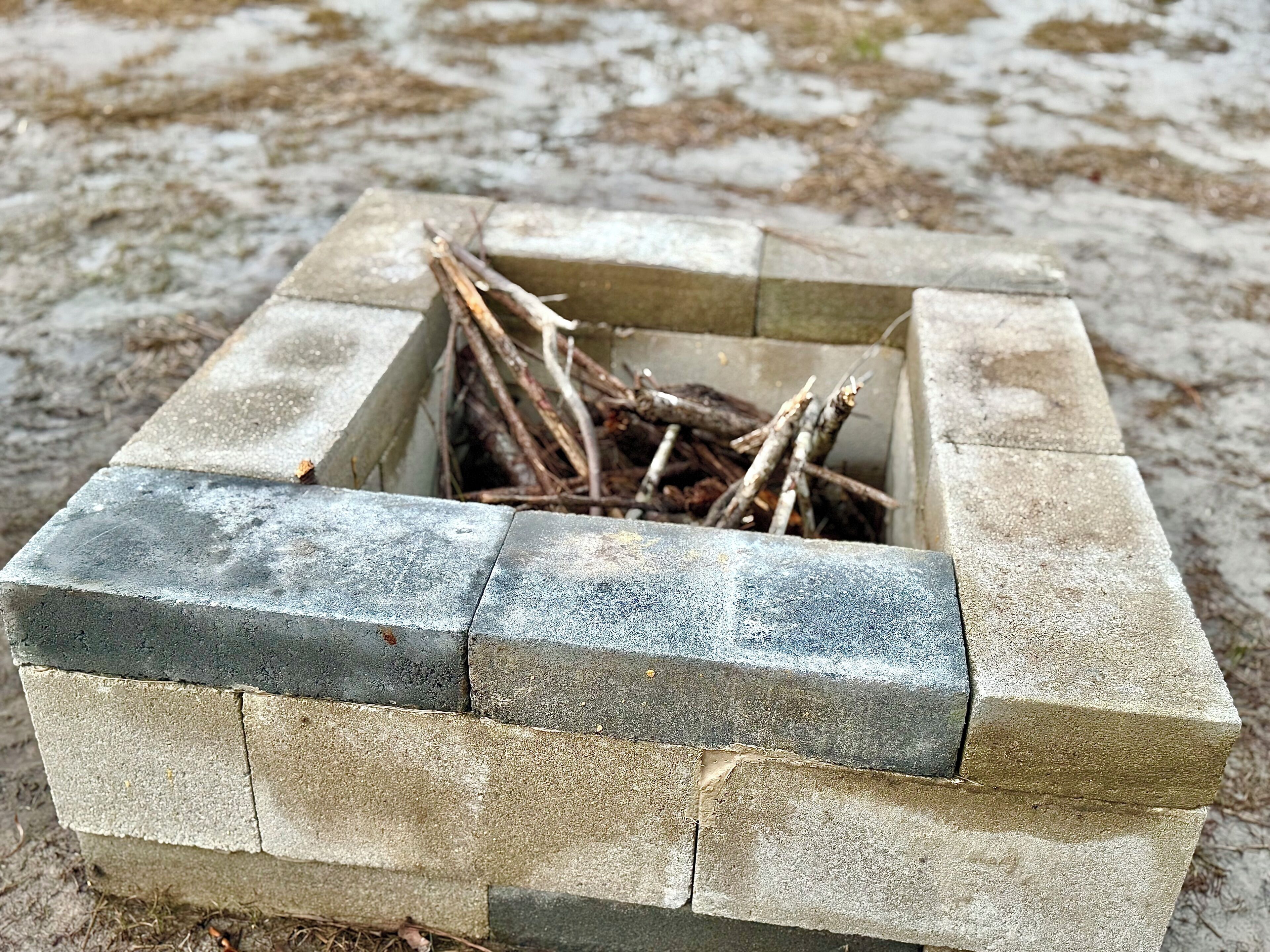 A concrete fire pit with logs inside, surrounded by a square stone border.