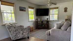 A living room with a zebra-patterned armchair, a grey sofa, a wooden floor, a ceiling fan, and a TV on the wall.