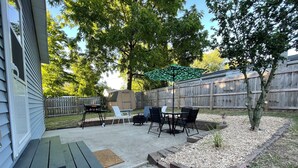 A backyard patio with a grill, outdoor furniture, and a wooden fence.