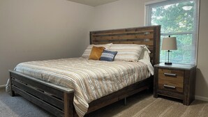 A bedroom with a wooden bed, a nightstand with a lamp, and a window with blinds.