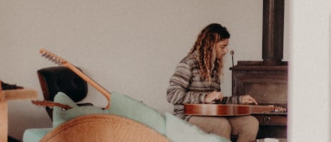 A person playing a guitar in a room with a wooden cabinet and a chair.