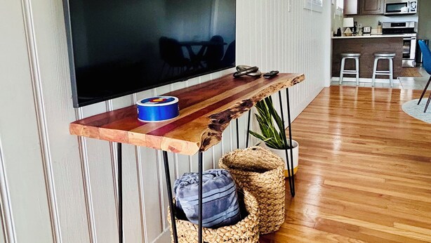 Un salon moderne avec un téléviseur à écran plat fixé sur un meuble TV en bois, une cuisine en arrière-plan et un coin repas avec des tabourets.