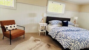 Une chambre à coucher comprenant un lit, une chaise, une table de chevet, une lampe et une fenêtre avec des stores.