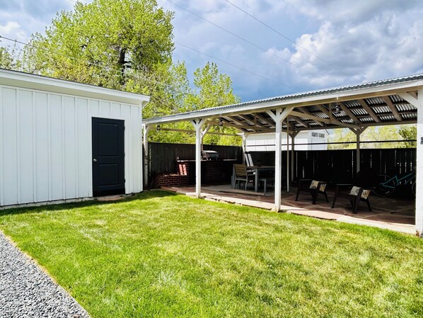 Ein überdachter Patio-Bereich mit Grill, Sitzgelegenheit und einem kleinen Schuppen.