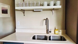 Une cuisine dotée d’un évier à deux bacs, de meubles blancs et d’étagères où sont rangés de la verrerie et des tasses.