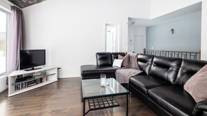 Ein modernes Wohnzimmer mit einem schwarzen Ledersofa, einem Glastisch und einer weißen Unterhaltungseinheit mit Flachbildfernseher.