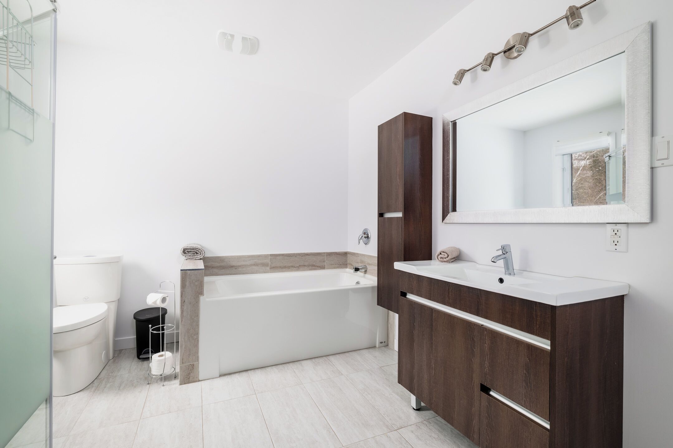 A modern bathroom with a bathtub, two sinks, and a large mirror.