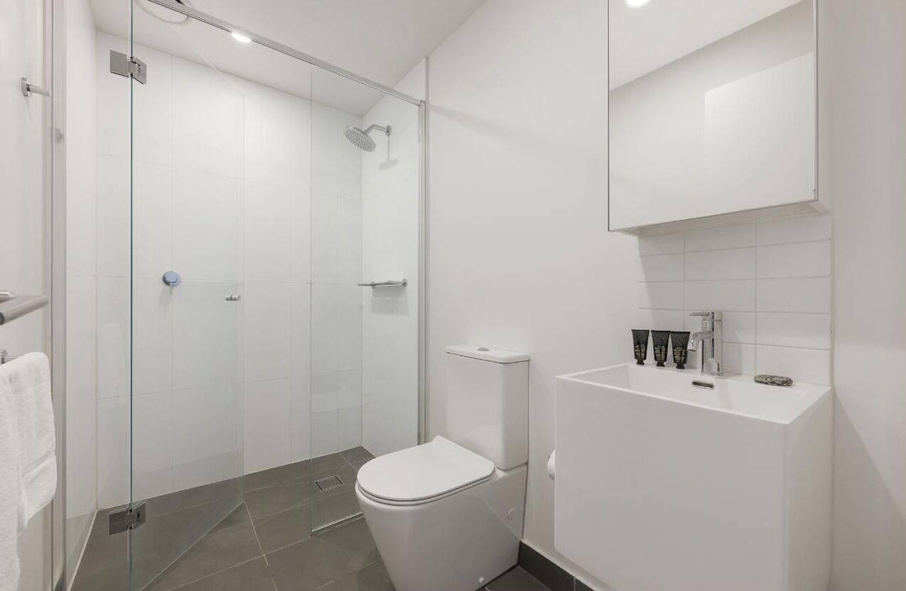 Une salle de bain moderne avec une douche à parois de verre, des toilettes blanches et un lavabo agrémenté d’articles de toilette.