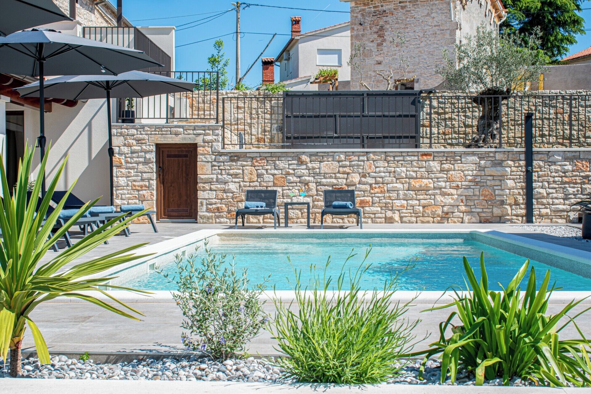 A pool area with stone walls, a wooden door, and outdoor seating.