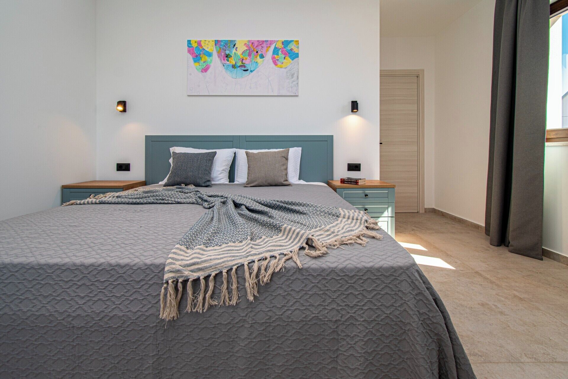 Een slaapkamer met een bed, nachtkastjes, een kunstwerk aan de muur en een deur.