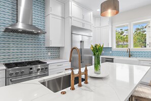 A modern kitchen with white cabinetry, a stainless steel range, a copper faucet, and a view of the outdoors through a window. - Shore Thing | Private Pool | Walk to the beach | Bike to Seaside | Brand New Construction and Decor (Santa Rosa Beach)