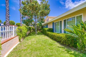 Una propiedad residencial con césped cuidado, una cerca blanca de piquetes y un gran árbol.