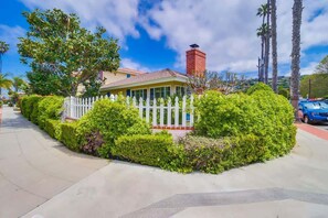 A house with a white picket fence, surrounded by lush greenery and a clear sky.