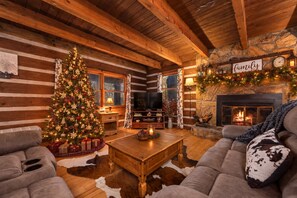 A cozy log cabin interior with a Christmas tree, a fireplace, and rustic furnishings.
