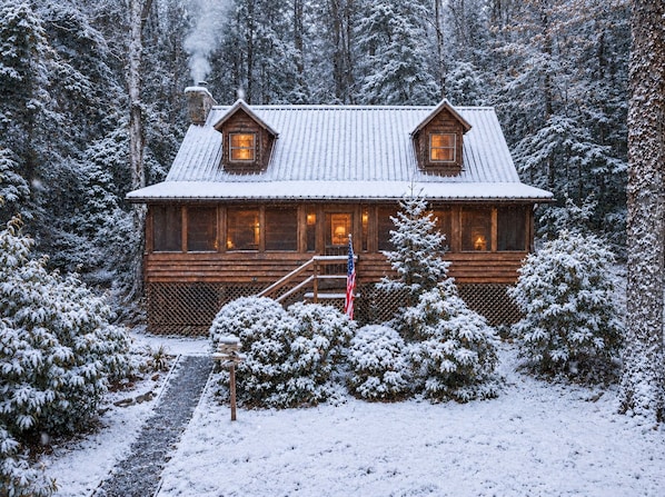 A wooden cabin with a snow-covered roof, surrounded by trees.