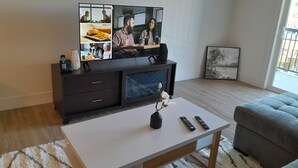 Una sala de estar moderna con un televisor de pantalla plana, una mesa de centro con un jarrón y controles remotos, un sofá gris y una obra de arte enmarcada en la pared.