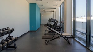 Un gimnasio moderno con equipo de levantamiento de pesas, una banca y un amplio ventanal con vista a la ciudad.