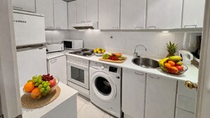 Una cocina moderna con armarios blancos, microondas, estufa, lavadora y pileta.