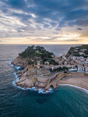 An aerial view of a coastal town with a fortified structure, a beach, and a rocky coastline.