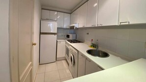 Cocina compacta con armarios blancos, microondas, lavabo y lavadora.