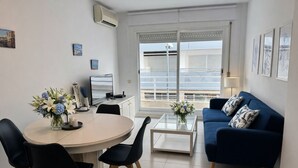 Una sala moderna con una mesa redonda de comedor, dos sillas negras, un sofá azul y un balcón con vistas.
