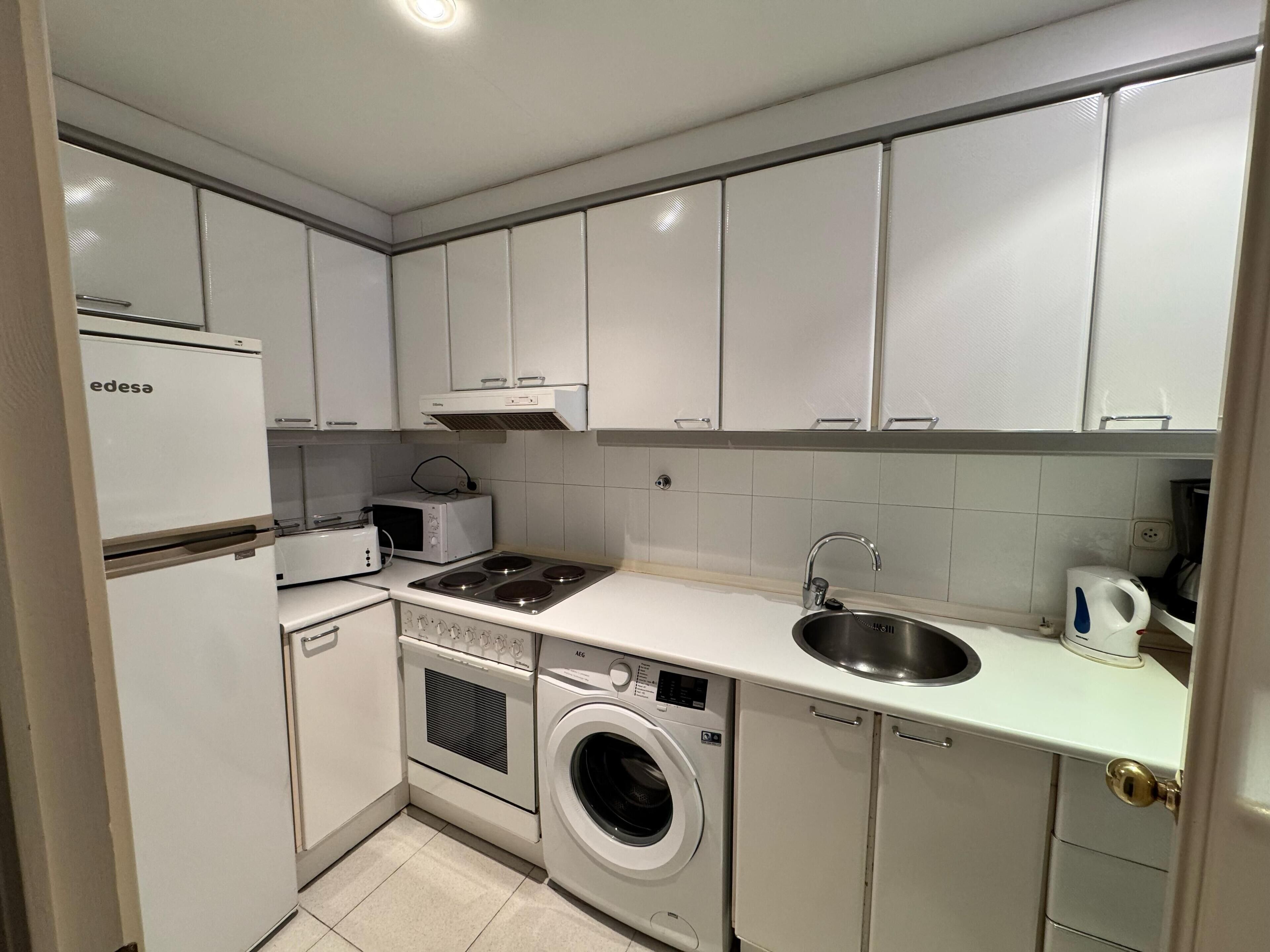 A compact kitchen with white cabinets, a built-in microwave, a stove, a sink, and a washing machine.