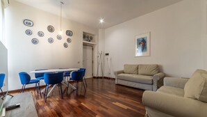Una sala de estar con piso de madera, un sofá, una mesa de comedor con sillas y platos decorativos en la pared.