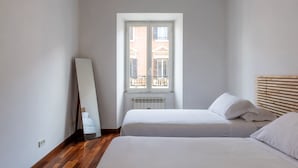 Un dormitorio minimalista con dos camas, un ventanal grande y un radiador.