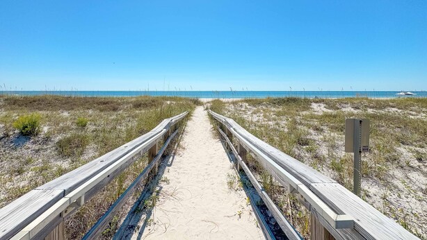 A wooden boardwalk leading to a beach with a clear sky. - CHARMING COTTAGE ON THE BEACH! (Gulf Shores)