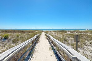 A wooden boardwalk leading to a beach with a clear sky.