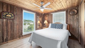 A bedroom with a wooden ceiling, a bed, two bedside lamps, a window, and a wall sign. - CHARMING COTTAGE ON THE BEACH! (Gulf Shores)