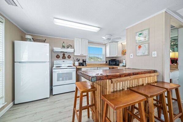 A kitchen with a central island, white appliances, and a view to the outside.
