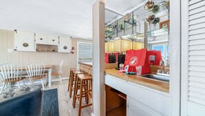 A modern kitchen with white cabinets, a wooden countertop, and a glass display shelf. There are red bags on the counter and a sink with a faucet. - CHARMING COTTAGE ON THE BEACH! (Gulf Shores)
