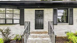 Een huis met twee verdiepingen, een zwarte voordeur, een witte bakstenen gevel en zwarte luiken.
