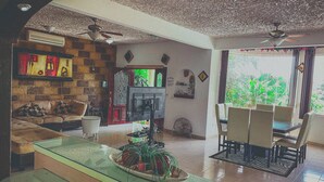 A living room with a glass coffee table, a sofa, a dining area with chairs, a ceiling fan, and a view of greenery outside. - Casa Bonita in Santa Fe (Xochitepec)