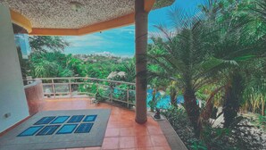 A covered outdoor area with a tiled floor, a metal railing, and a view of lush greenery and a distant landscape. - Casa Bonita in Santa Fe (Xochitepec)