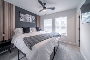 Een slaapkamer met een bed, een plafondventilator en twee ramen met zonwering.