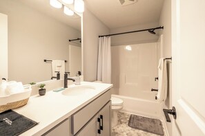 Een moderne badkamer met een witte wastafel, een spiegel, een klein plantje, een handdoekhouder en een douchegordijn.