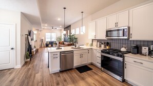 A modern kitchen with white cabinets, stainless steel appliances, and a wooden floor. - Game Room! Modern 3BR 2.5BA New Build Luxury—Near Downtown Cleveland! (Cleveland)